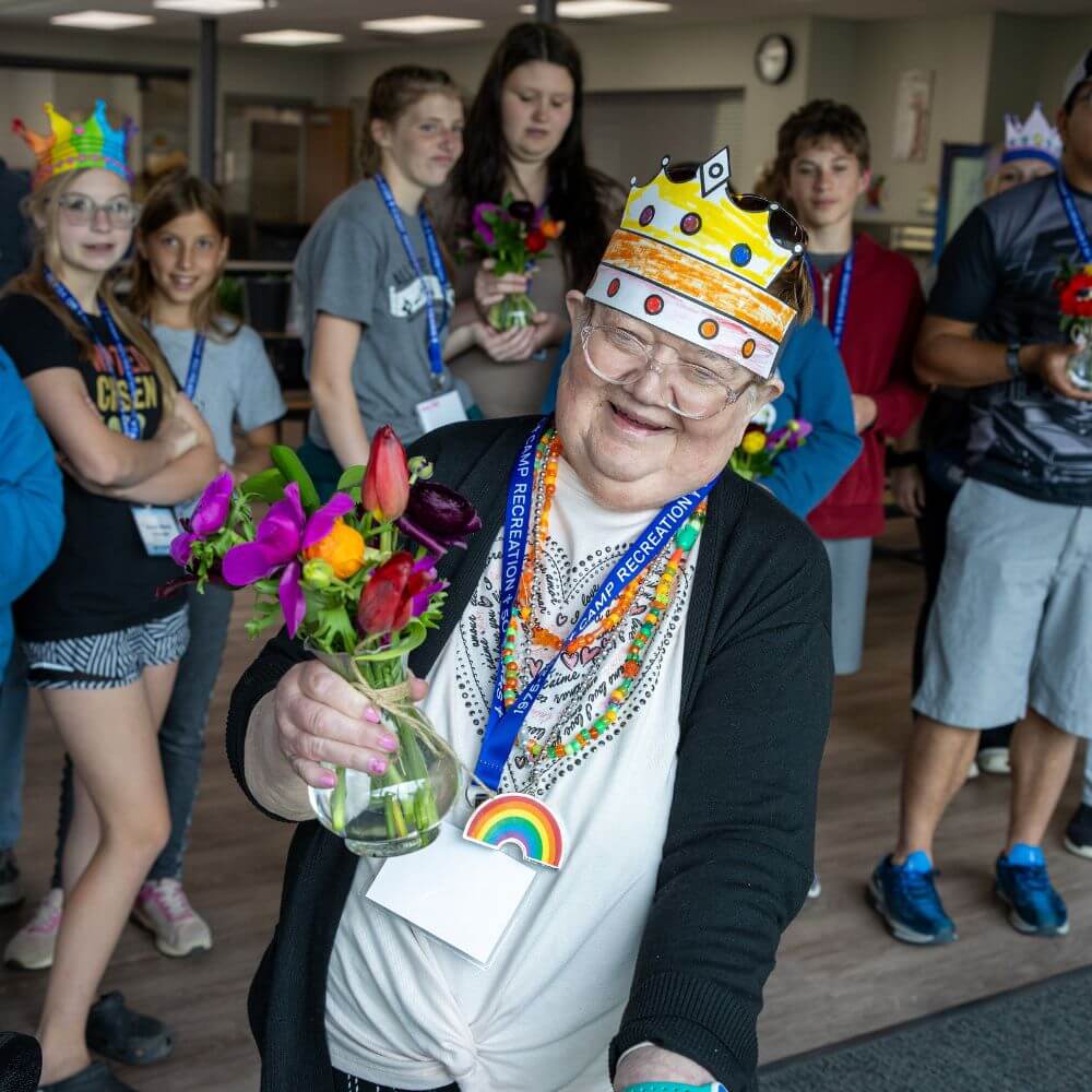 Camper smiling wearing paper crown and holding bouquet of flowers at Camp ReCreation