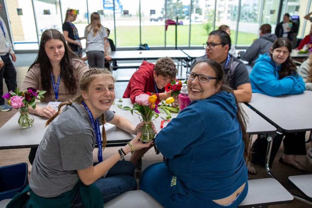 Group of campers and counselors sitting table creating flower bouquets at Camp ReCreation