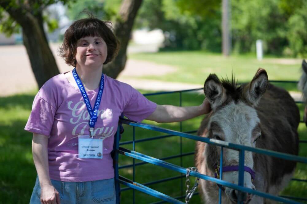 Female camper petting donkey outside at Camp ReCreation