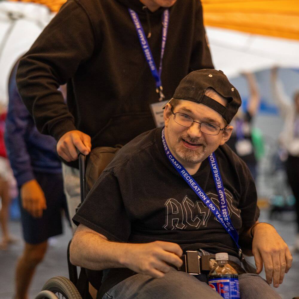 Volunteer pushing camper in wheelchair at Camp ReCreation
